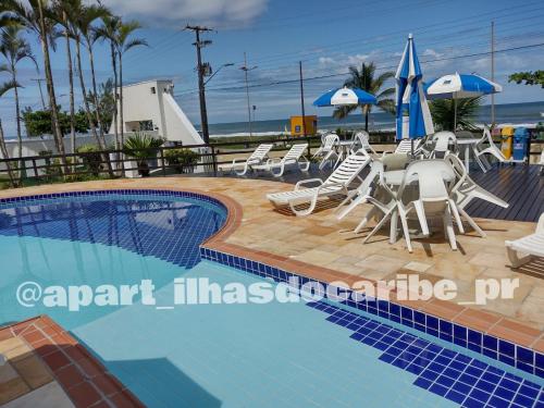 a swimming pool with chairs and umbrellas next to the beach at Apto Cond Ilhas do Caribe - Pr - Beira Mar in Matinhos