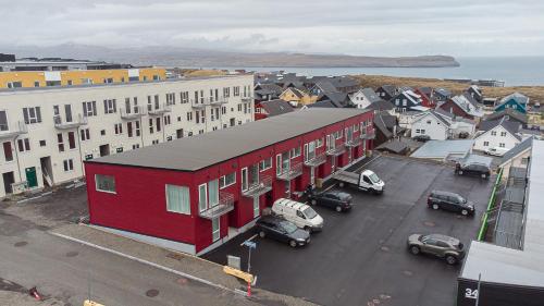 a red building with cars parked in a parking lot at New Three Bedroom Townhouses with Sea View in Tórshavn