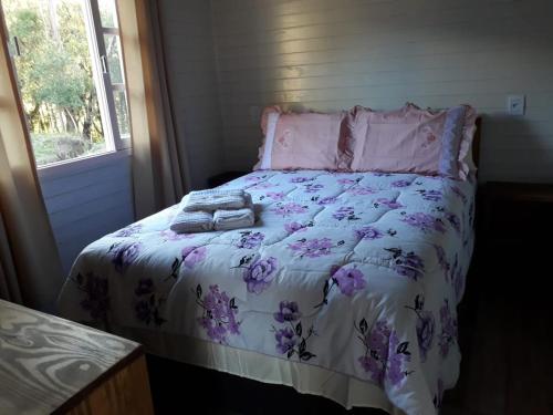 a bed with a purple and white comforter and a window at Pousada Cabanas Flor de Mel in Urubici