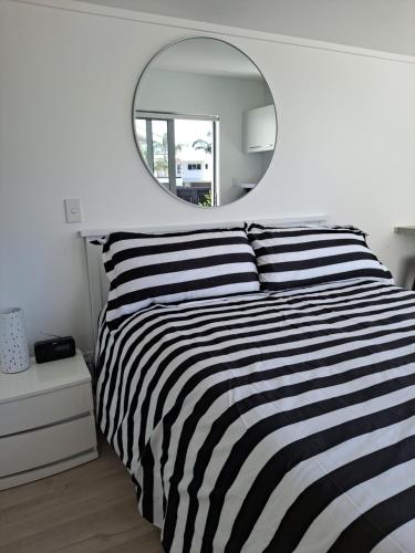 a bedroom with a black and white striped bed and a mirror at Pod bach on Tweed in Tauranga