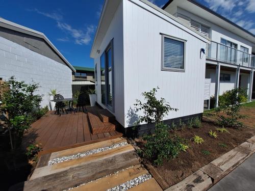 een wit huis met een houten terras bij Pod bach on Tweed in Tauranga