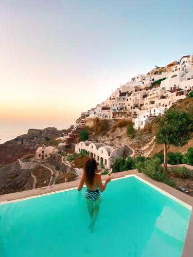 a woman sitting on the edge of a swimming pool looking at a village at Old Castle Oia in Oia