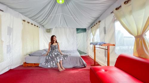 uma mulher sentada numa cama numa tenda em แสงเหนือแคมป์ปิ้งม่อนแจ่ม em Ban Mae Raem