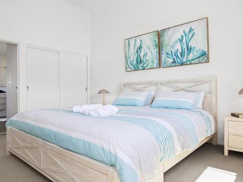 a white bedroom with a large bed with blue pillows at Bay Views in Callala Bay