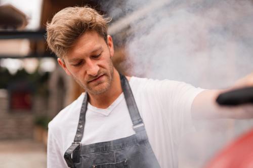 a man in an apron is cooking in a stove at Hotel Viktoria & Landhaus Joggl in Mayrhofen