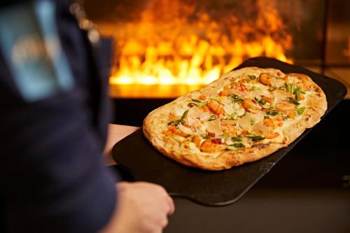 a person holding a pizza on a table with a fireplace at Hotel Die Krone - Immenstadt-Stein in Immenstadt im Allgäu