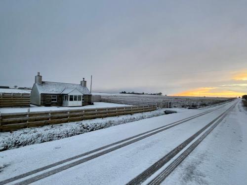 a snow covered road with a house and a fence at Taigh Neonach in Watten