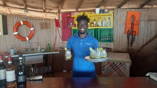 un homme debout dans un bar tenant un plateau de boissons dans l'établissement African Ecolodge Angurman, à Bruce