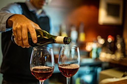 a man pouring red wine into two wine glasses at Хотел Том и Нези Класик in Velingrad