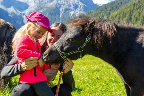 two girls and a woman petting a small pony at Hotel Bella Vista in Trafoi