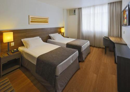 a hotel room with two beds and a desk at Premier Copacabana Hotel in Rio de Janeiro