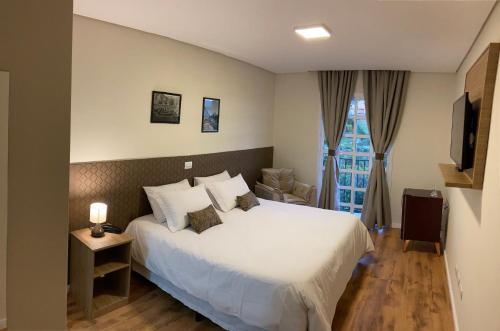 a bedroom with a large white bed and a chair at Village de Charme - 2km do Capivari in Campos do Jordão
