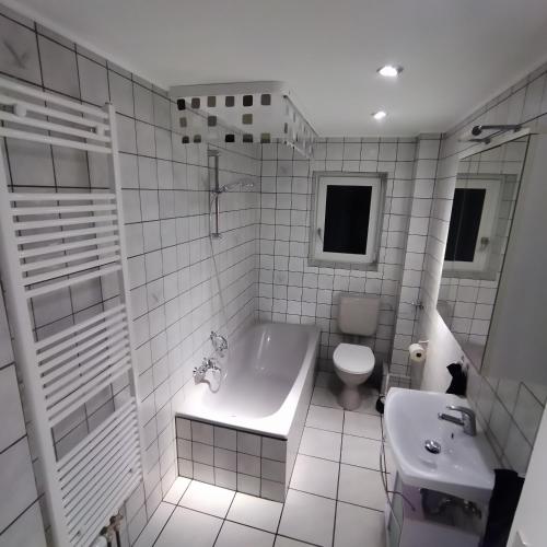 a white tiled bathroom with a tub and a toilet at Wohnung Neunkirchen 2 in Neunkirchen am Brand