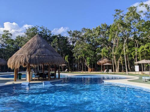 a swimming pool with a straw umbrella and a resort at 2-Bedroom Condo by the Jungle w/ Swimming pool in Puerto Morelos