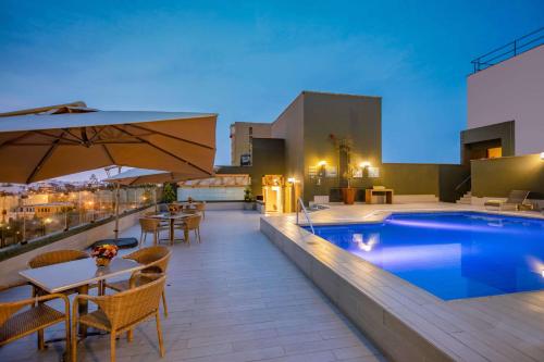 um pátio no último piso com uma piscina, mesas e cadeiras em Sonesta Hotel El Olivar em Lima