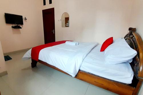 a bedroom with a bed with white sheets and red pillows at RedDoorz Syariah near Komplek Candi Arjuna Dieng 2 in Dieng
