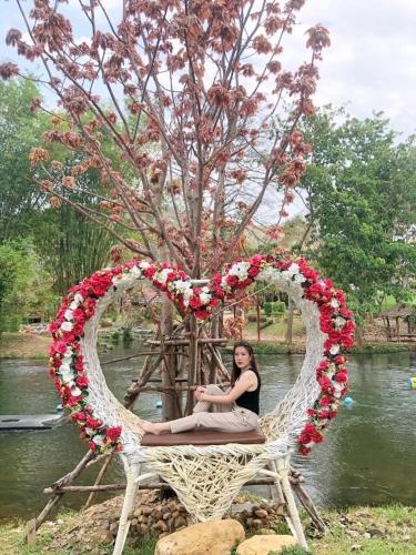 a woman sitting in a heart shaped chair next to a tree at JK Riverview Resort in Ban Song Phi Nong