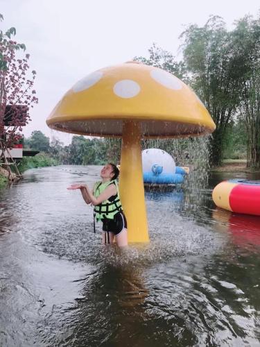 a woman is standing in the water in a giant mushroom at JK Riverview Resort in Ban Song Phi Nong