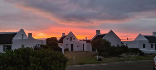 a group of white houses with a sunset in the background at Casa Pescador Beach House in Struisbaai