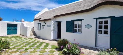 a white house with a gray roof and blue doors at Casa Pescador Beach House in Struisbaai