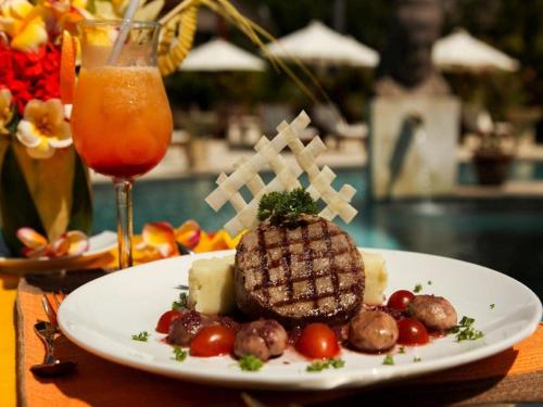 einen Teller mit Fleisch und Gemüse und einem Getränk in der Unterkunft Siddhartha Oceanfront Resort & Spa Bali in Tulamben