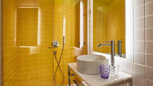 a yellow tiled bathroom with a sink and a shower at Mama Shelter Paris La Défense in Puteaux