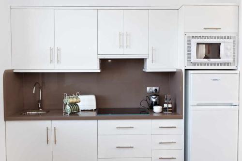 a white kitchen with white cabinets and a microwave at Casa Vagón Vía Verde de la Sierra in Olvera