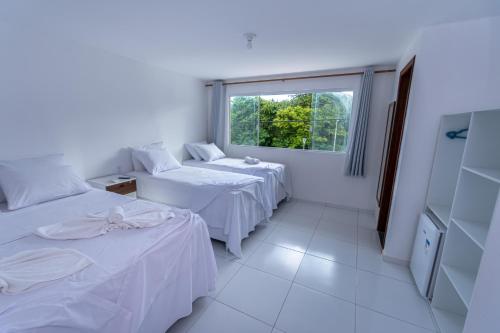 two beds in a white room with a window at Hotel do Pescador in Morro de São Paulo