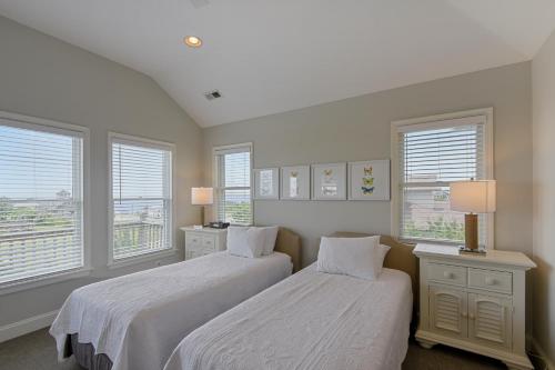 two beds in a bedroom with two windows at The Sanderling in Duck