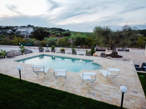 a swimming pool with four chairs and a tree at Quattroperle Trulli - Relax - Puglia in Castellana Grotte