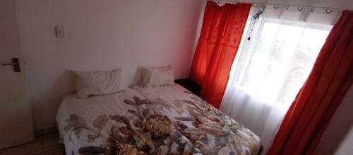 a bedroom with a bed and a window with red curtains at sandpiper in Jeffreys Bay