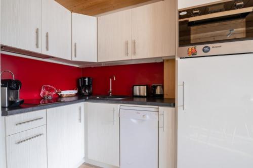 uma cozinha com armários brancos e uma parede vermelha em Comfortable studio with terrace and mountain views em Megève