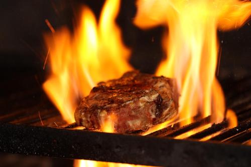 a piece of meat cooking on a grill with flames at Auberge Aal Veinen in Vianden