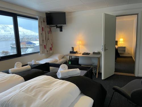 um quarto de hotel com três camas, uma secretária e uma janela em Hotel Runavík em Runevig