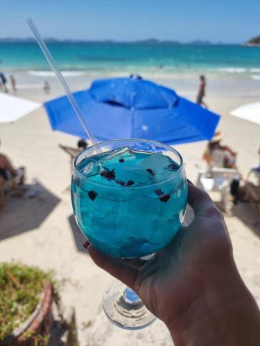 a hand holding a blue drink in front of the beach at Pousada Seven in Arraial do Cabo