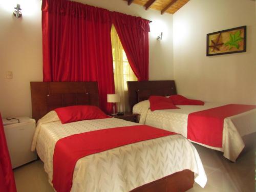 two beds in a room with red curtains at Hotel Campestre Pueblo Bello in Armenia