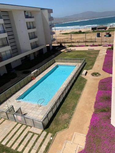 a swimming pool next to a building and the beach at Departamento a pasos de playa Los Molles in Los Molles