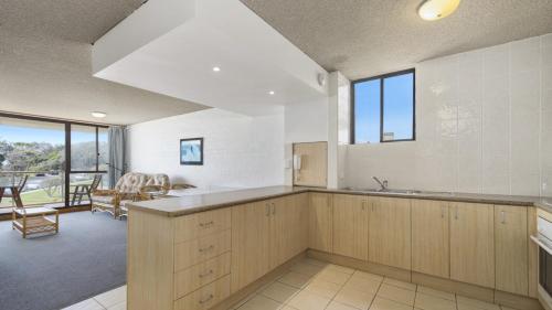 a kitchen with wooden cabinets and a living room at 15 Beachpark Apartments in Port Macquarie