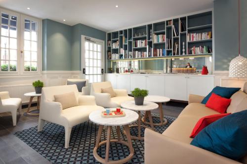 a living room with chairs and tables and bookshelves at Hôtel des 3 Poussins in Paris
