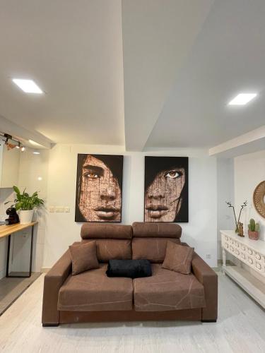 un sofá marrón en una sala de estar con dos fotos en A Das Marías ESTUDIO, en Ourense