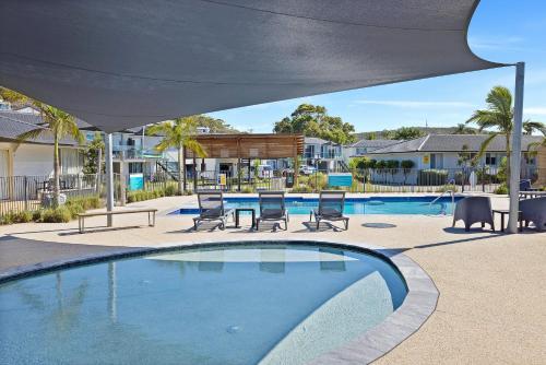 a swimming pool with chairs and a table and an umbrella at Seaside Holiday Resort in Fingal Bay