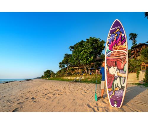 a person standing on the beach with a surfboard at Nirvana Beach Resort, Koh Lanta SHA Extra Plus in Ko Lanta