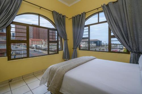 a bedroom with a bed and two large windows at Ushaka Holiday Apartments in Durban