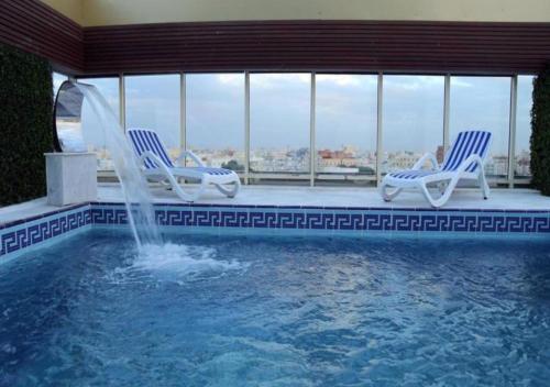 una piscina con 2 sillas y una fuente en Areen Hotel Airport en Yeda