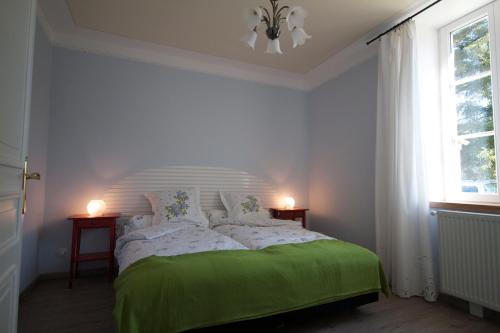a white bedroom with a green bed with two windows at Moulin de Merzé in Cortambert