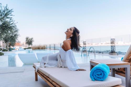a woman in a white dress sitting on a bench by a pool at Hyatt Centric Jumeirah Dubai in Dubai