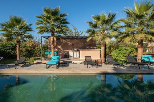 ein Pool mit Palmen und Stühlen daneben in der Unterkunft Les Iris - Peaceful villa with heated private pool & hammam in Marrakesch