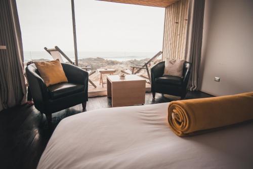 a hotel room with a bed and two chairs and a large window at Hotel 8 al Mar in Pichilemu