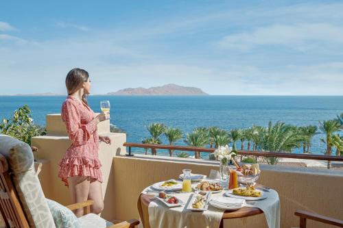 a woman standing on a balcony with a table with a glass of wine at Four Seasons Resort Sharm El Sheikh in Sharm El Sheikh