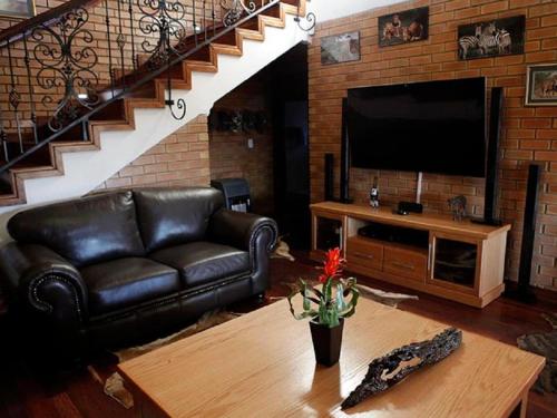 a living room with a black leather couch and a television at Lichenry Bush Lodge in Mokopane